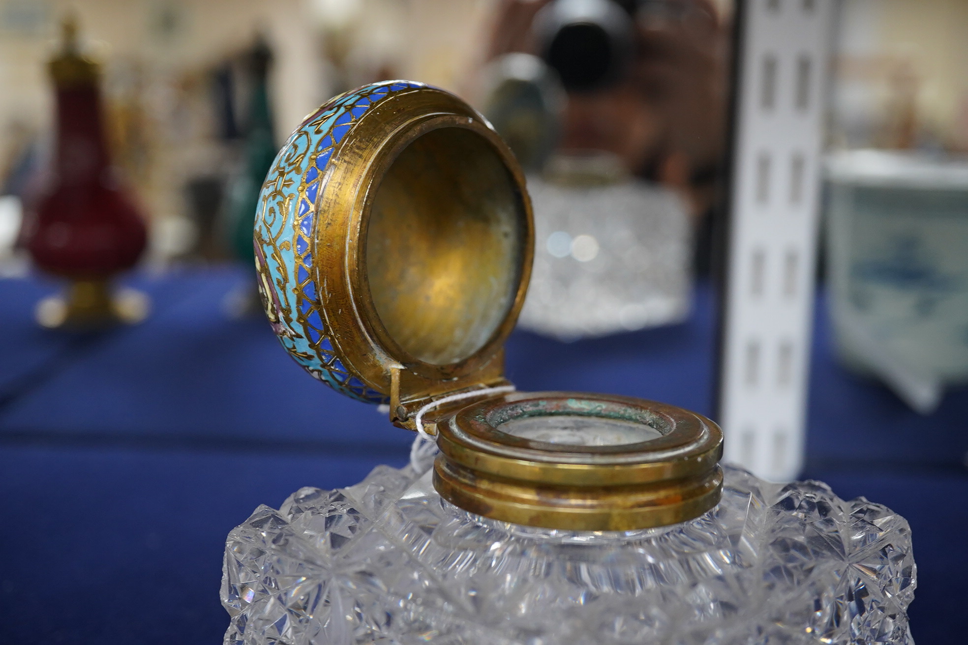 A large square glass inkwell, heavily cut with star cut base and octagonally cut top with enamelled brass hinged cover, 8cm wide. Condition - fair, some chipping